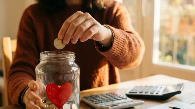 Person depositing coins in a charity jar with a heart next to a tax return form